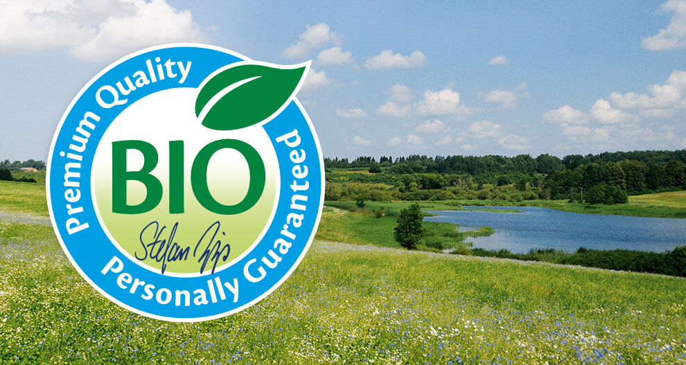 Een landschap met water, groen en een blauwe lucht is bedekt met een cirkelvormig logo met het woord "BIO" en de naam "CLAUS HIPP".