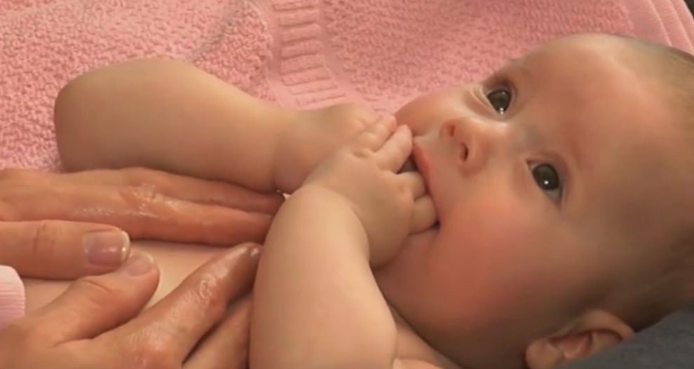 Een baby met handjes op het gezicht, liggend op een roze handdoek.