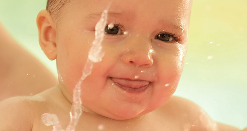 Het gezicht van een baby is gedeeltelijk ondergedompeld in water, met waterdruppels zichtbaar op de huid.