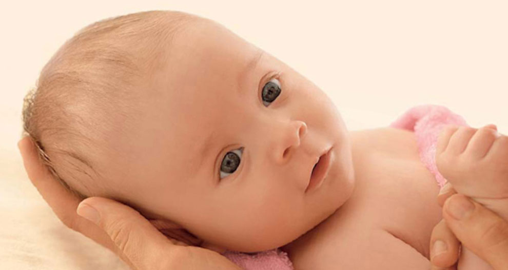 Een close-up van het gezicht van een baby, met een hand die zachtjes het hoofdje wiegt.