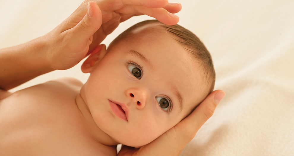 Een close-up van het gezicht van een baby, met een hand die zachtjes het hoofdje wiegt.
