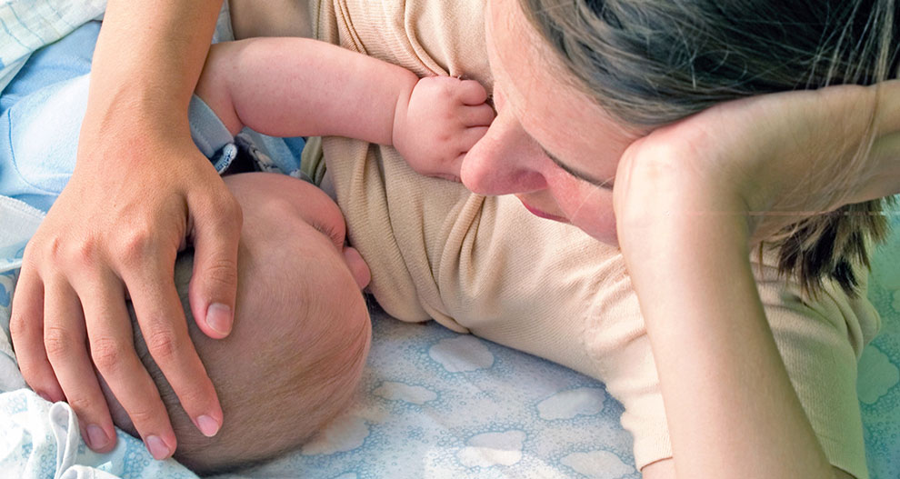 Een vrouw wiegt het hoofd van een baby op een stof met patroon.
