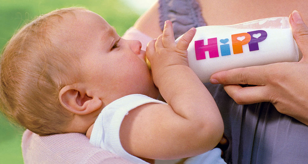 Een baby drinkt uit een flesje met het woord "HiPP" erop.