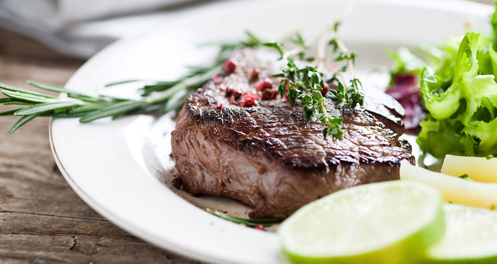 Een steak met rozemarijn- en tijmgarnituur, geserveerd met een groene salade en schijfjes limoen.