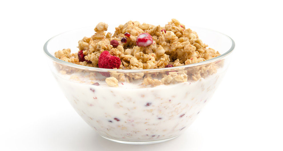 Een transparante kom gevuld met granola en rode bessen, gedeeltelijk ondergedompeld in een witte vloeistof.
