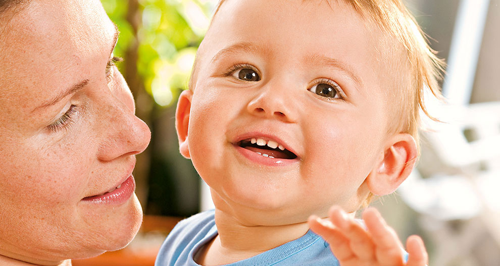 Een close-up van een vrouw en een baby. De vrouw kijkt omlaag naar de baby, die glimlachend omhoog kijkt.