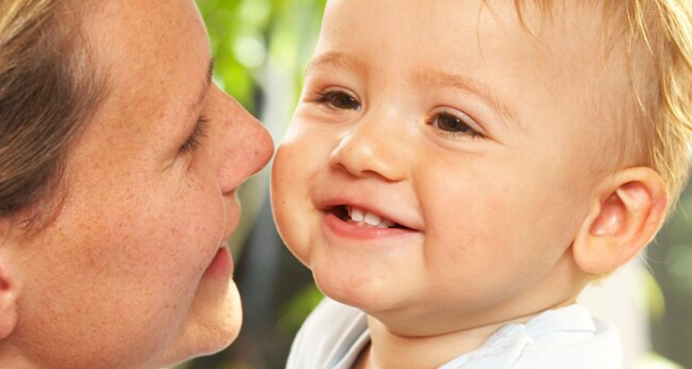 Een close-up van een vrouw en een baby, met het gezicht van de vrouw gedeeltelijk zichtbaar en het gezicht van de baby volledig in beeld, kijkend naar elkaar.