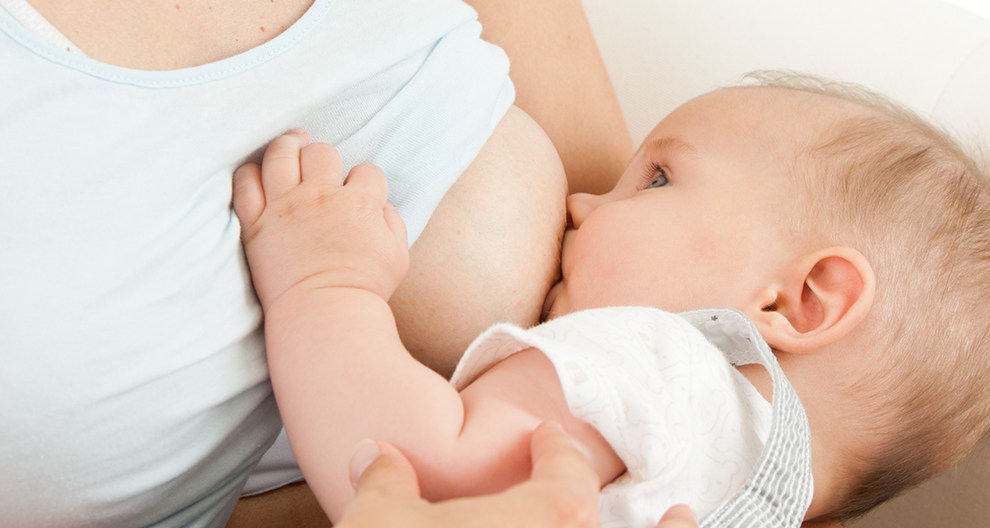Een close-up van het gezicht van een baby, met één oog zichtbaar, terwijl hij borstvoeding krijgt van een vrouw.