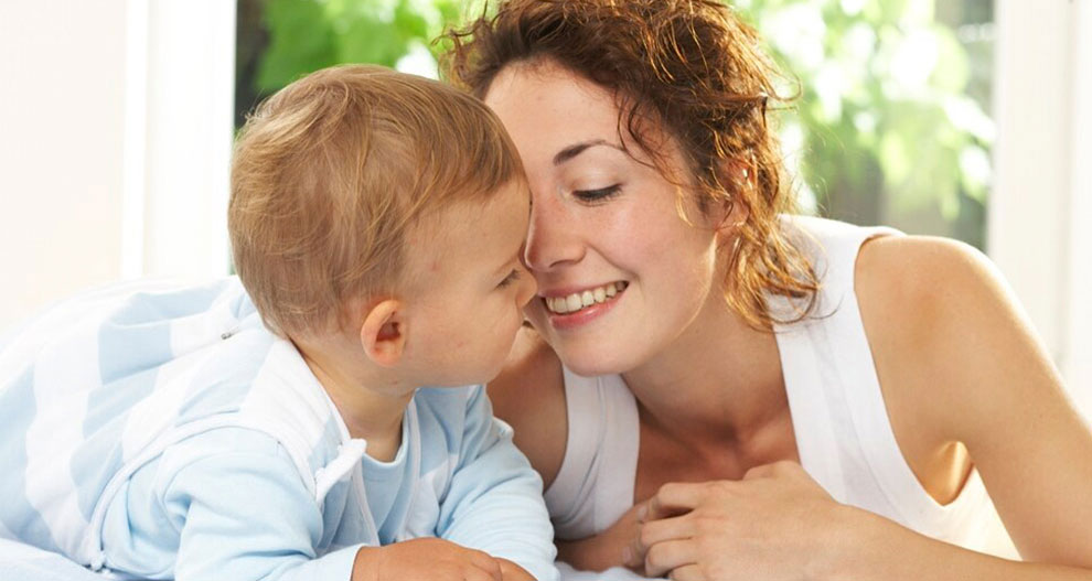 Een vrouw en een baby liggen op een bed. De vrouw kijkt liefdevol naar de baby.
