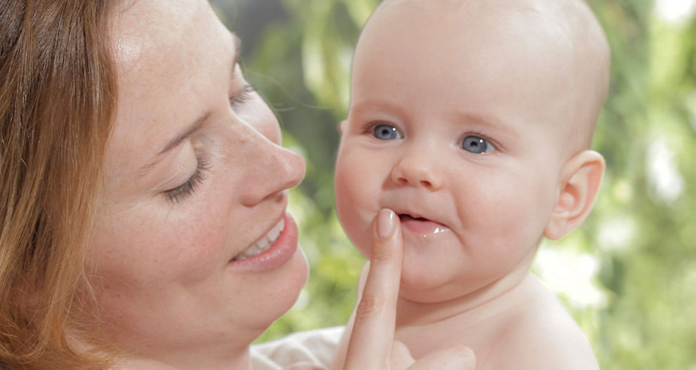 Een vrouw houdt een baby vast, die in de vinger van de vrouw bijt.