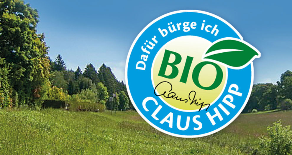 Een landschap met bomen en gras is bedekt met een blauw cirkelvormig logo met het woord "BIO" en de naam "Claus Hipp".
