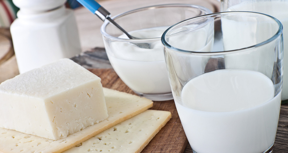 Een glas melk, een kom yoghurt, kaas en crackers op een houten tafel.