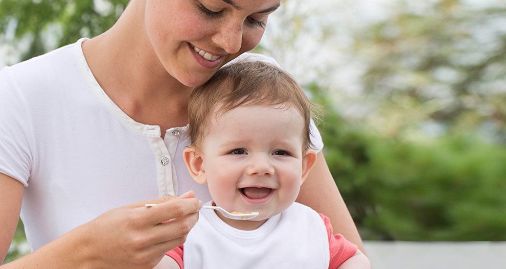 Een vrouw in een wit shirt voedt een baby met een lepel.