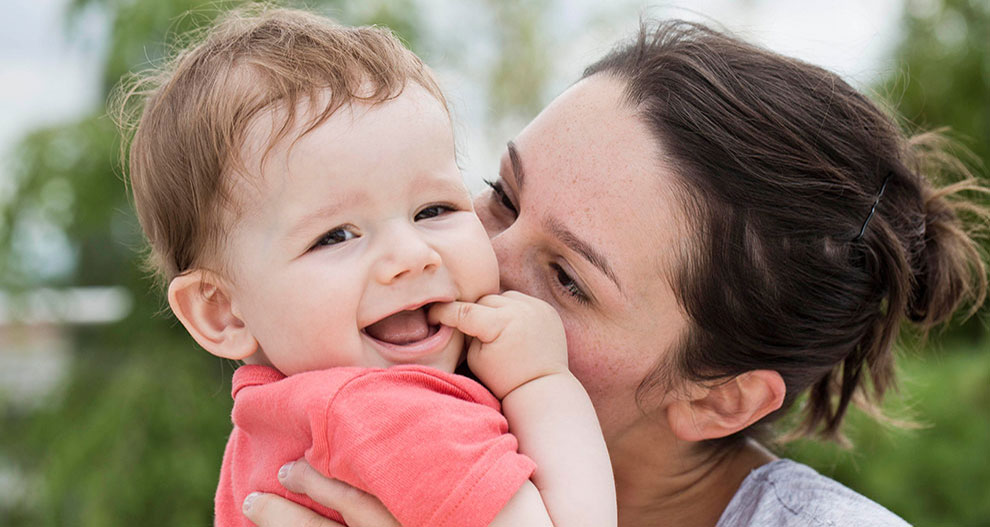 Een vrouw houdt buiten liefdevol een lachende baby vast.