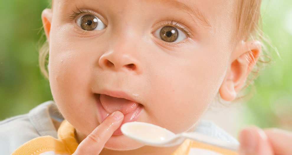 Een close-up van het gezicht van een baby, met een lepel eten in de buurt van de mond, vastgelegd in een open moment.