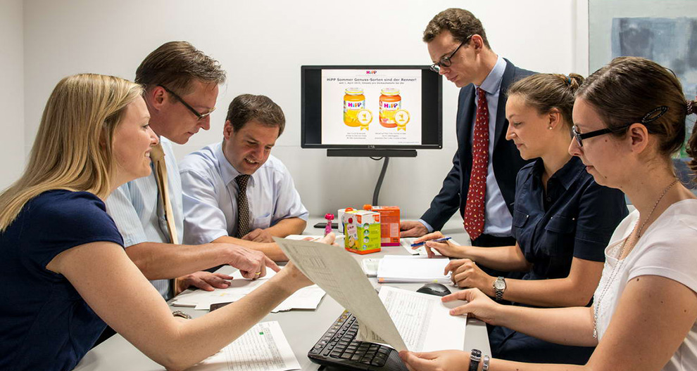 Een groep professionals vergadert over een presentatie op een computerscherm met een product met het label "MIP".