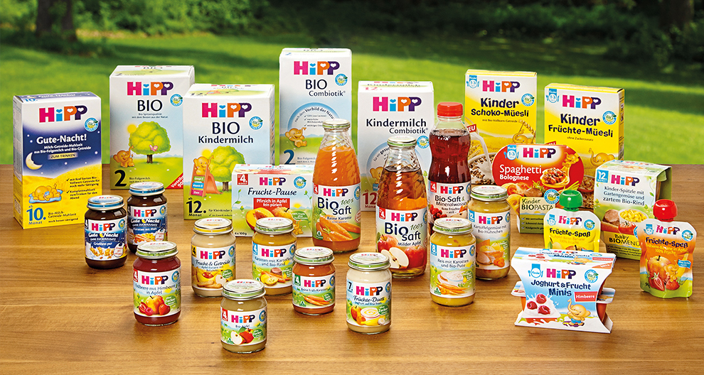 Diverse Hipp babyvoedingsproducten uitgestald op een tafel met een groene buitenachtergrond.